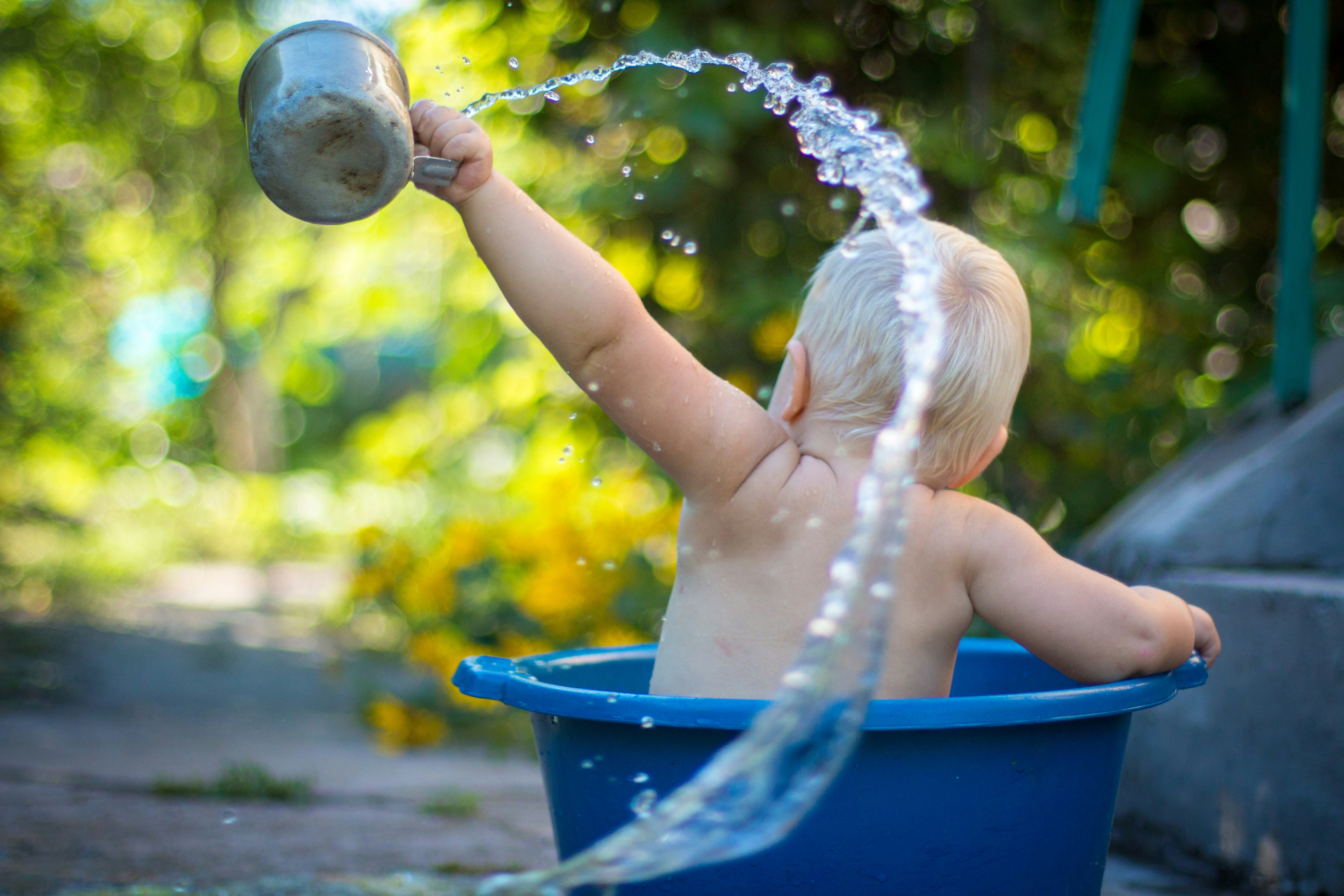 Baby back seated in a blue bucket playing with water